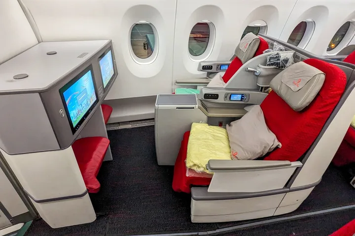 Red Ethiopian Airlines business class seat with pillow, blanket, and IFE screen inside aircraft cabin.