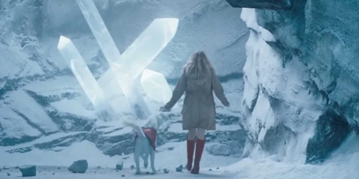 A woman and dog walk toward glowing ice crystals in a snowy, fantastical cave setting.