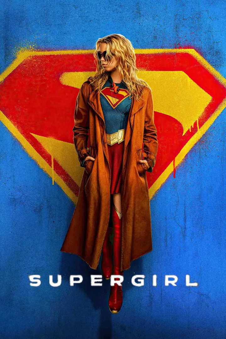A woman in Supergirl costume and trench coat poses before a graffiti Superman logo.