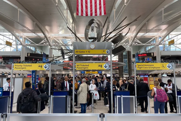 Busy airport security checkpoint with TSA PreCheck lanes, priority and general passenger queues under American flag.