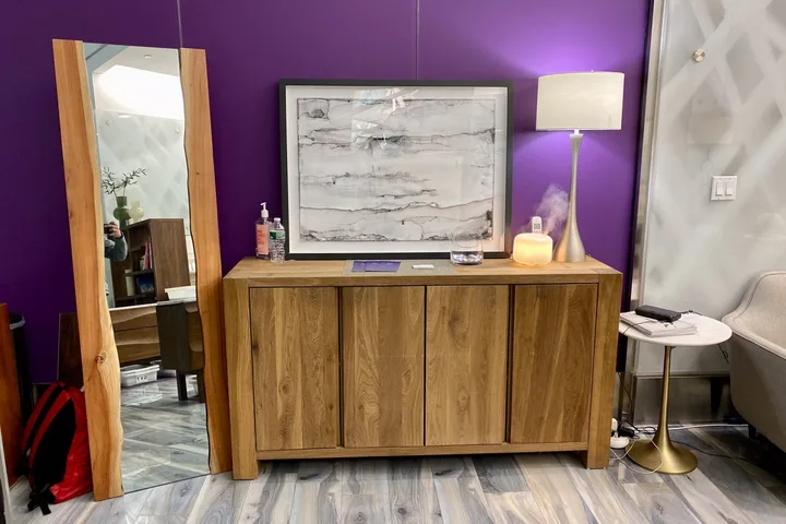 Upscale lounge interior with purple accent wall, wooden credenza, framed art, and lamp in a modern room.