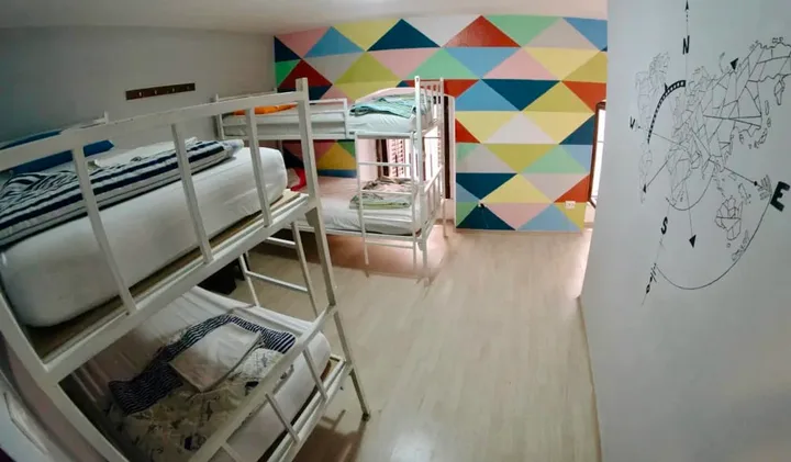 Bright hostel dorm room with white bunk beds and a vibrant geometric multicolored accent wall.