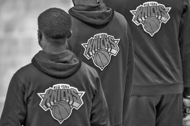 Three people wearing New York Knicks hooded sweatshirts viewed from behind in black and white.