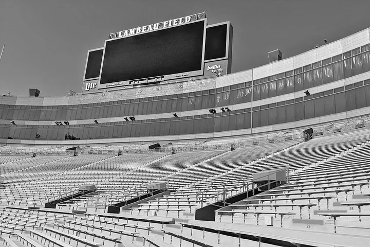 Empty Lambeau Field stadium interior with seating rows and scoreboard visible in black and white.