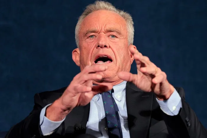 RFK Jr. speaking animatedly with both hands raised against a dark blue background.