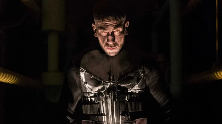 Jon Bernthal as the Punisher in dark skull armor, lit dramatically from below in a shadowy corridor.