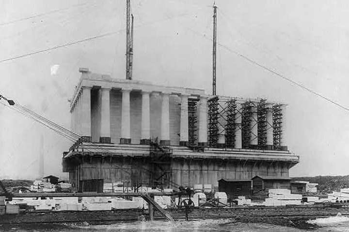 Historic black-and-white photo of the Lincoln Memorial under construction with scaffolding and cranes.