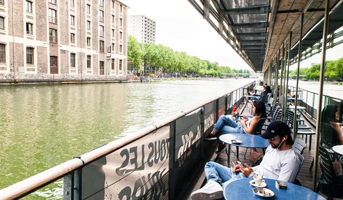 People relaxing at an outdoor waterfront cafe terrace along a Paris canal.