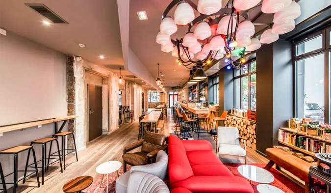 Stylish hostel common room with red sofas, eclectic lighting, and bar area.