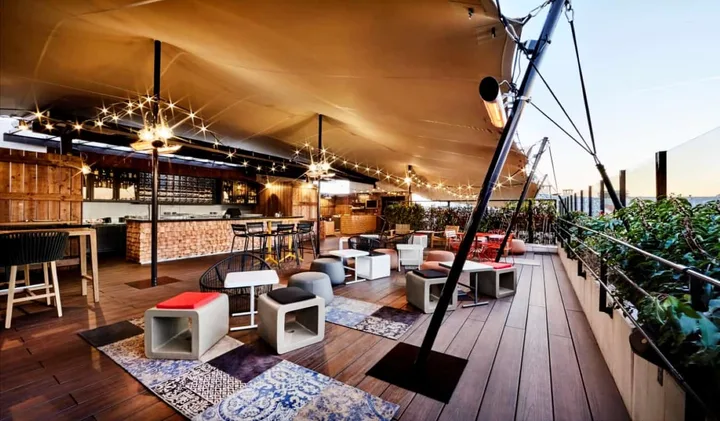 Rooftop bar terrace with string lights, lounge seating, and city views at dusk.