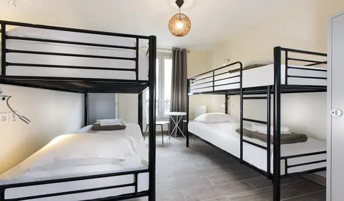 Bright hostel dorm with black metal bunk beds, white linens, and a pendant lamp.
