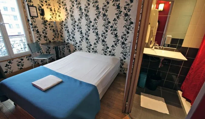 Small private hostel room with floral wallpaper, single bed, and en-suite bathroom.
