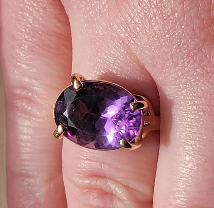 Close-up of a large oval amethyst gemstone in a rose gold prong setting worn on a finger.