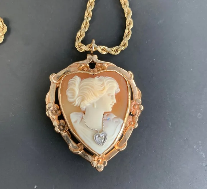 An antique heart-shaped gold cameo pendant on a rope chain, featuring a woman's profile with floral frame.