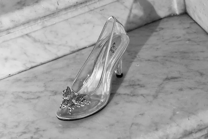 A clear glass slipper with butterfly embellishment resting on a marble surface, black and white photo.