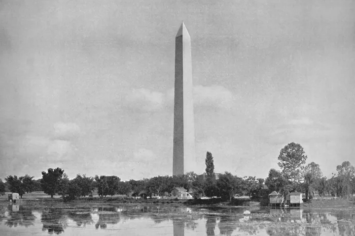 Vintage black-and-white photo of Washington Monument reflected in surrounding marshy water.