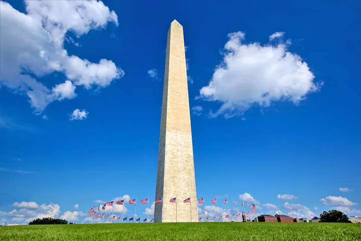 Washington Monument surrounded by American flags under a bright blue sky, low-angle view.
