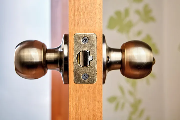 Close-up of antique brass door knobs and latch mechanism on a wooden door edge.