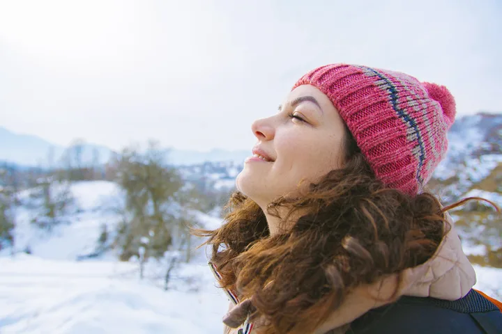 Young woman in pink winter hat breathing fresh air outdoors in a snowy mountain landscape.