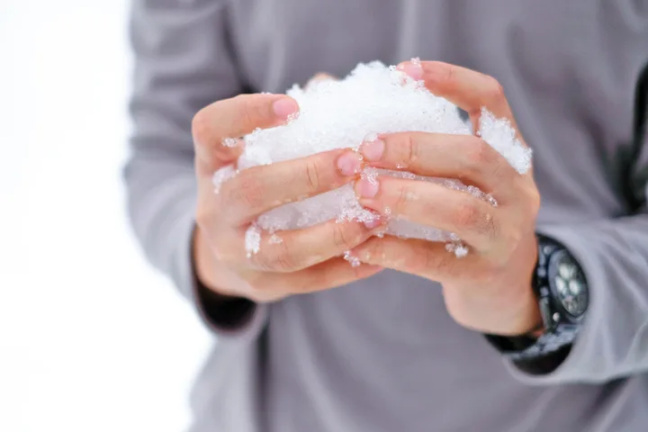 Close-up of hands holding a packed snowball in a white winter environment.