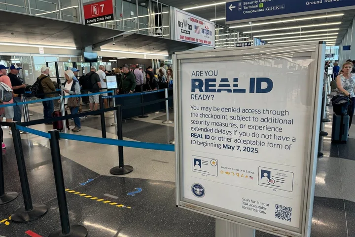 REAL ID readiness sign at a busy airport security checkpoint with travelers in line.