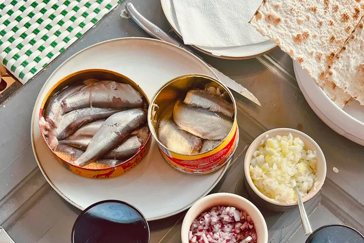 Two open cans of surströmming (fermented herring) on a plate with chopped onions and flatbread.