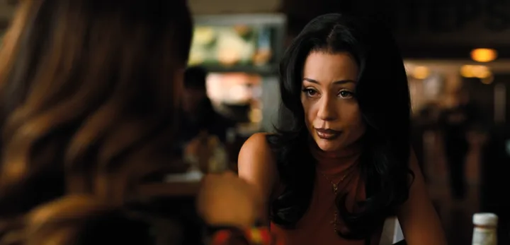 Dark-haired woman listening with a serious expression across a table in a dim diner, TV scene.