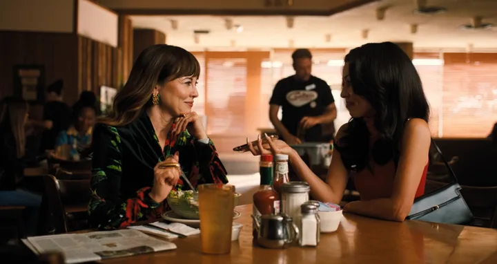 Two women sitting across from each other at a diner table, smiling and engaged in conversation, TV scene.