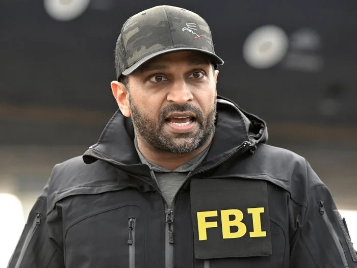 Man in FBI tactical jacket and camo cap speaking outdoors with a serious expression.