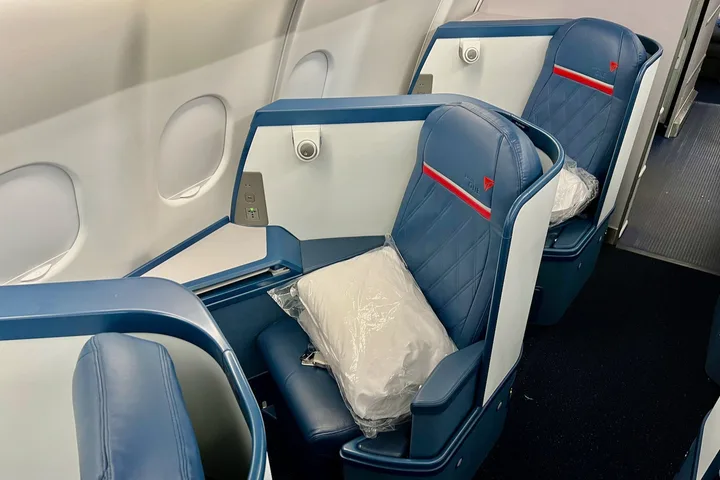 Close-up of a single Delta business class seat in blue leather with red accent stripe and wrapped amenity kit.