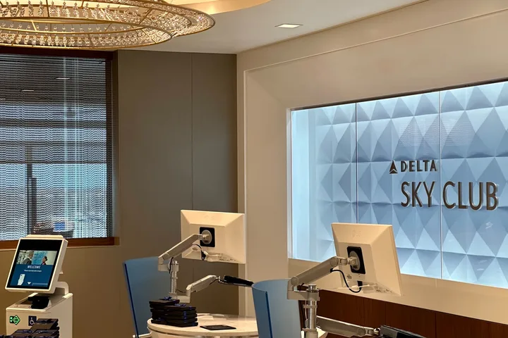Delta Sky Club check-in desk with monitors under a chandelier and illuminated Delta Sky Club signage.