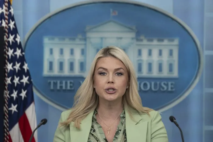 Blonde woman in green blazer speaking at White House press briefing podium with US flag.