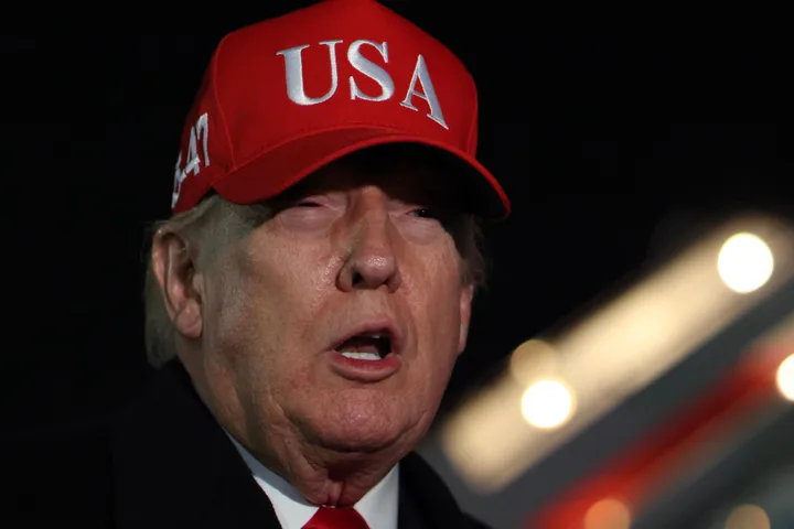 Man in red USA cap speaking outdoors at night against dark background.