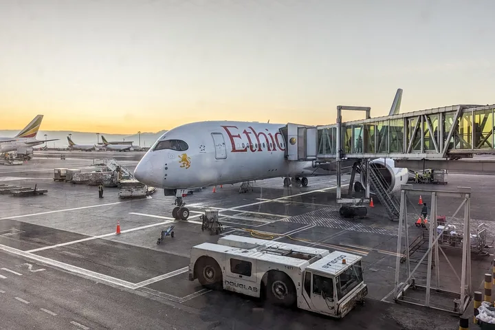 Ethiopian Airlines A350 aircraft parked at gate on tarmac at sunset with jet bridge attached.