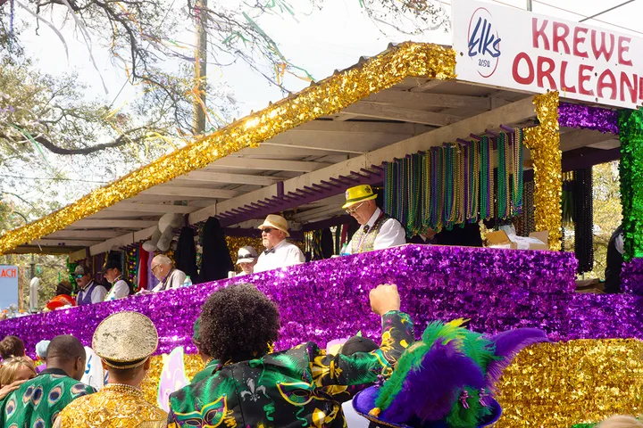 A glittering Krewe of Orleans parade float covered in purple and gold sequins with riders tossing beads.