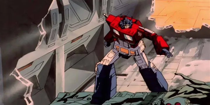 Animated Optimus Prime stands battle-damaged in a destroyed environment in classic 1986 style.