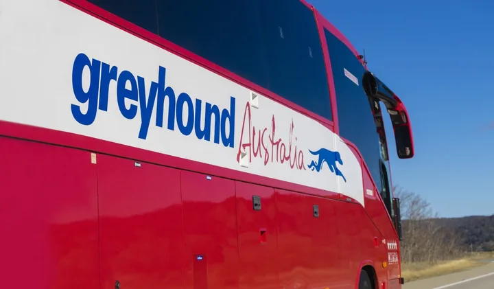 Close-up of a red Greyhound Australia coach bus parked outdoors under clear blue sky.