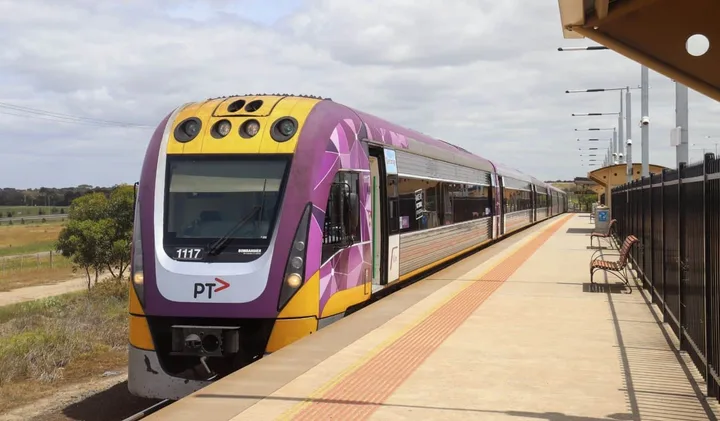 A purple and yellow Victorian PT train stopped at a rural Australian station platform.
