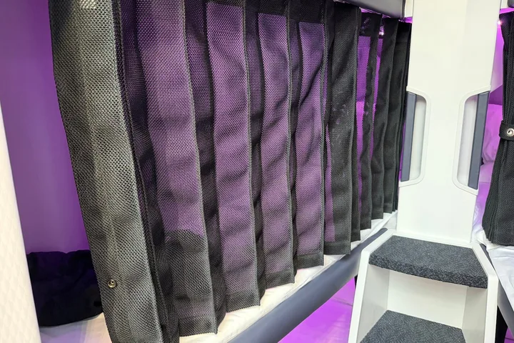 Close-up of black mesh privacy curtains drawn across airplane sleep pod berths with purple lighting behind.