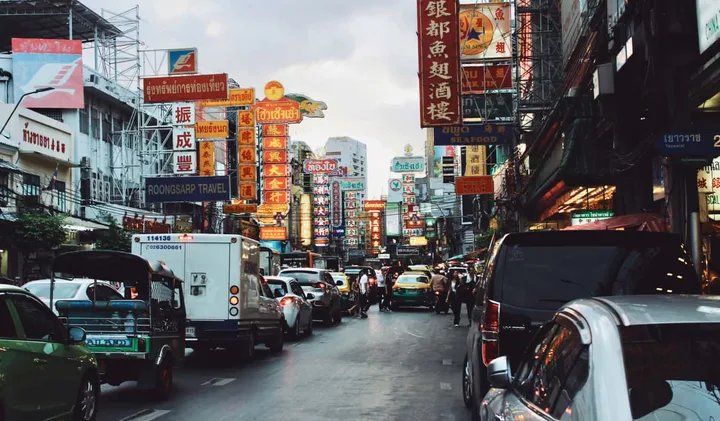 Busy Chinatown street in Bangkok lined with Chinese signage, tuk-tuks, and heavy traffic.