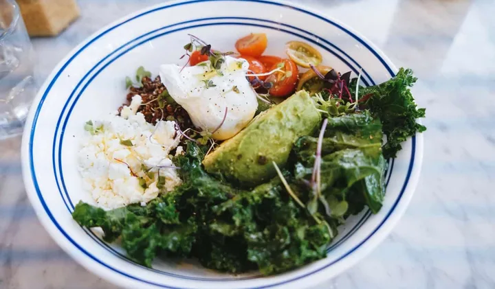 Healthy grain bowl with kale, avocado, poached egg, tomatoes, and feta.