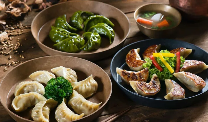Three bowls of assorted dumplings and gyoza on a rustic wooden table.