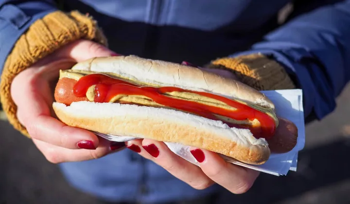 Person holding a street hot dog with ketchup and mustard outdoors.