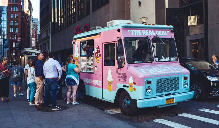 Pink ice cream truck labeled 'Frostie' with a line of customers on a NYC street.