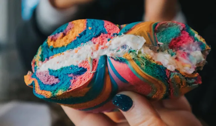 Hand holding a colorful rainbow bagel with cream cheese filling.