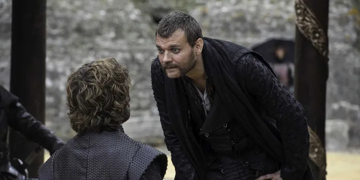 Two men in medieval costume having a tense confrontation outdoors against a stone wall.