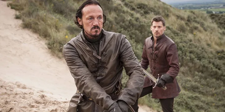 Two men in medieval costumes on sandy dunes, one holding a dagger.