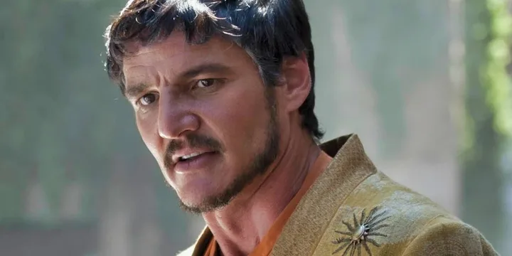 Dark-haired man in ornate gold and orange costume with a star brooch, intense expression.