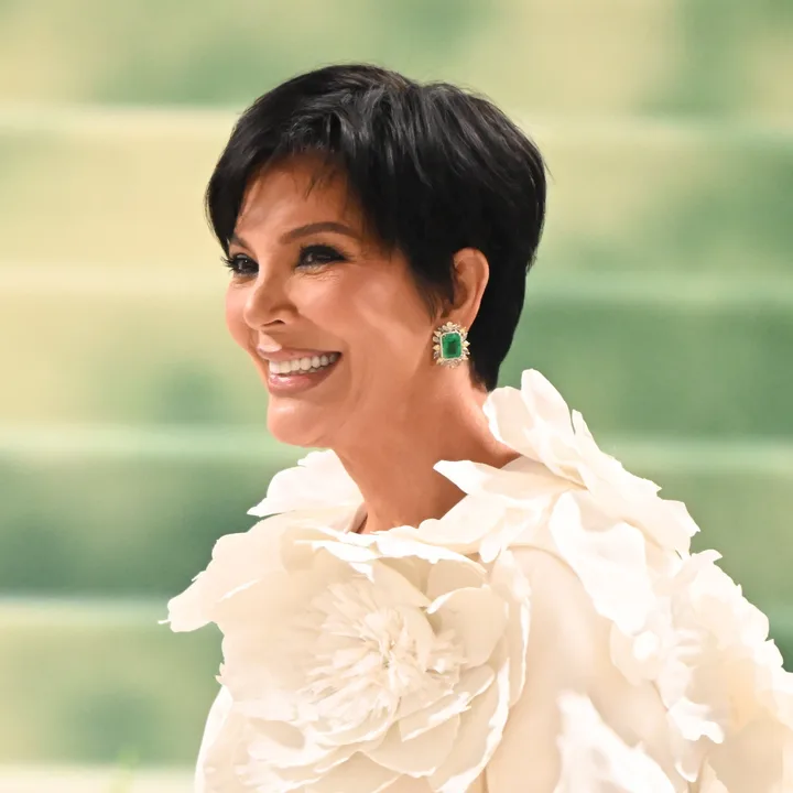 Kris Jenner smiling in a white floral gown at a glamorous event, short dark pixie cut.