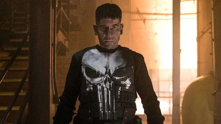 Jon Bernthal as the Punisher in full skull costume, standing in a darkly lit industrial setting.
